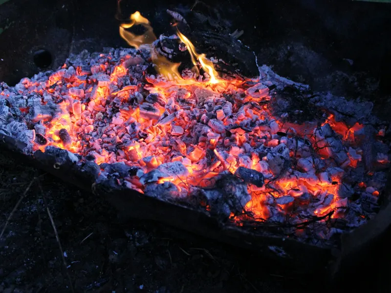 Brasero en tôle d'acier rempli de braises rougeoyantes et de flammes au crépuscule