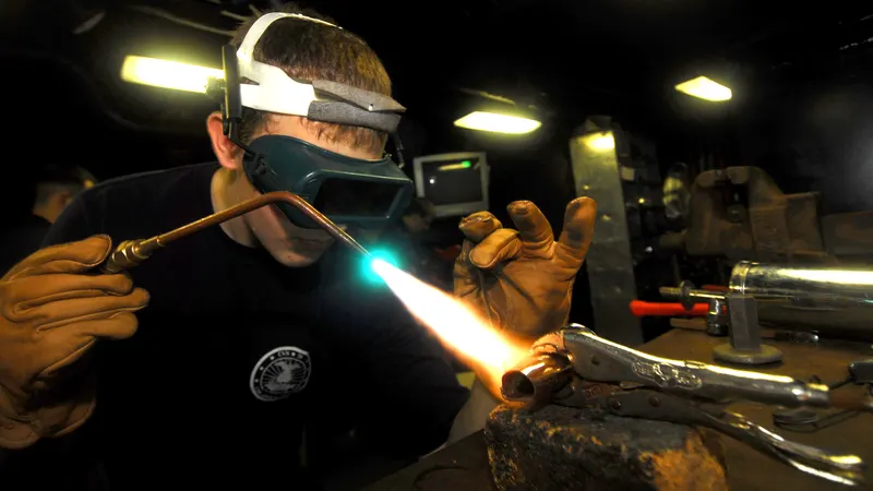 Opérateur avec lunettes de protection et gants de cuir chauffant un raccord au chalumeau oxyacétylénique