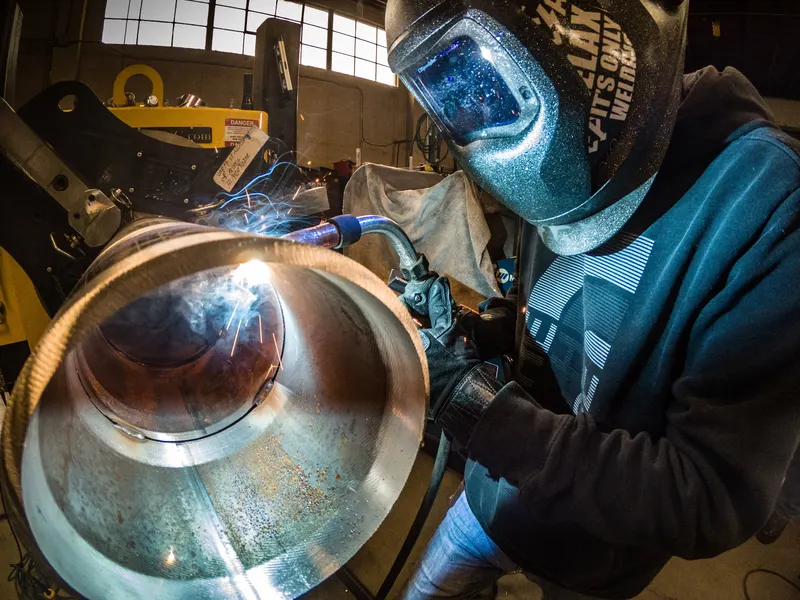 Soudeur casqué soudant au semi-automatique (MIG/MAG) l'intérieur d'un gros tube d'acier dans un atelier