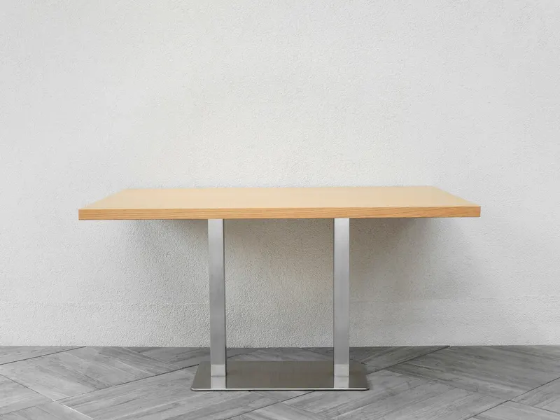 Table à plateau en bois sur un piètement central en acier brossé, posée contre un mur blanc